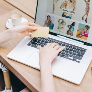 Hands holding a credit card while online shopping on a laptop at a wooden table.